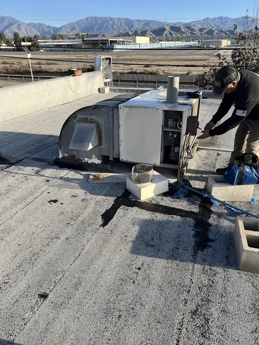 Technician servicing a rooftop HVAC unit with mountains in the background