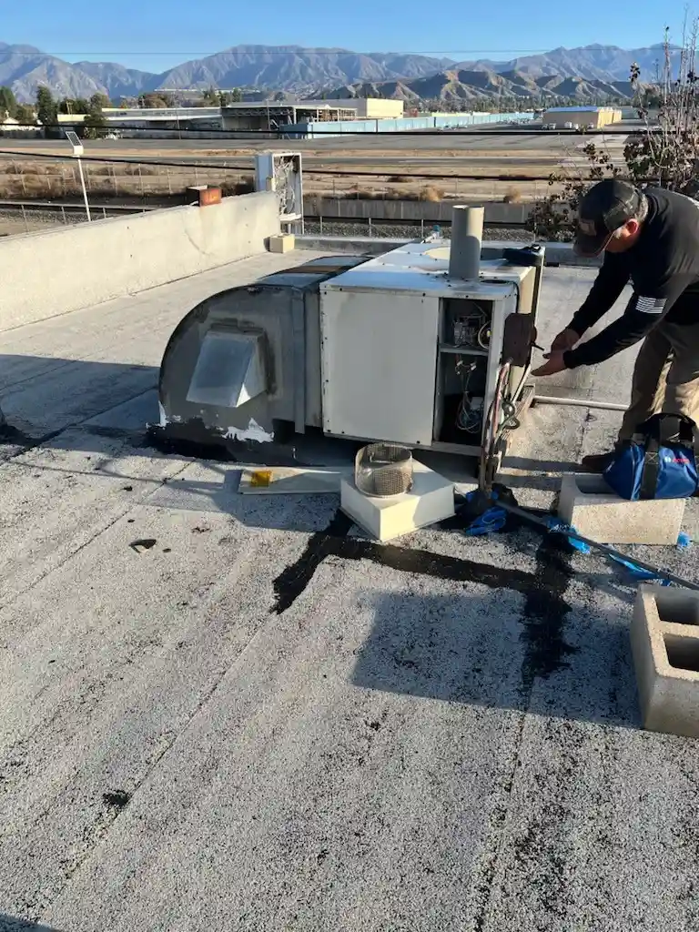 HVAC technician performing rooftop AC unit maintenance on a flat commercial building in Denver