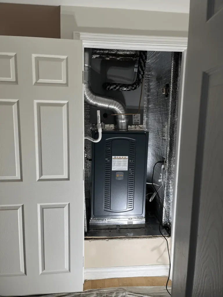 Residential furnace system installed in a utility closet, featuring insulated walls, air ducts, and a drain pipe